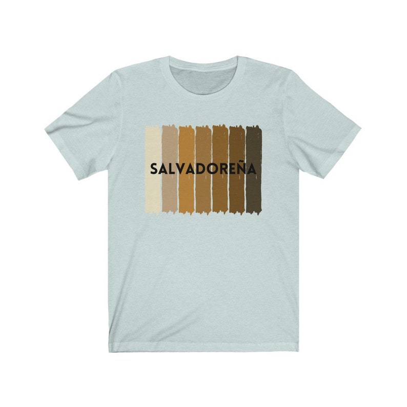 May include: Light blue t-shirt with a graphic of a horizontal stripe pattern in shades of brown and beige. The text "SALVADORE&Ntilde;A" is printed in black on the shirt.