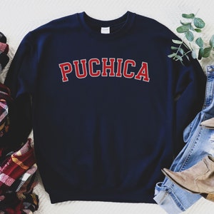 K&ouml;nnte beinhalten: Navyblauer Sweatshirt mit dem Wort "PUCHICA" in roten Buchstaben auf der Vorderseite.