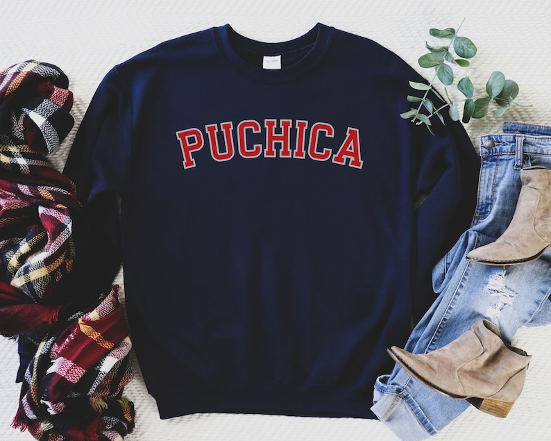 K&ouml;nnte beinhalten: Navyblauer Sweatshirt mit dem Wort "PUCHICA" in roten Buchstaben auf der Vorderseite.