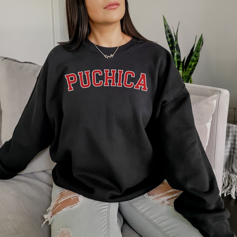 K&ouml;nnte beinhalten: Schwarzer Pullover mit roter Aufschrift "PUCHICA" auf der Vorderseite.