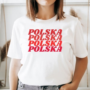 May include: White t-shirt with the word "POLSKA" repeated four times in red and pink lettering, stacked on top of each other.