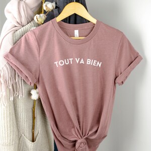 May include: A mauve colored t-shirt with the text "TOUT VA BIEN" in white lettering.