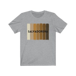 May include: A heather grey t-shirt with a graphic of a horizontal stripe pattern in shades of brown and beige. The text "SALVADORE&Ntilde;A" is printed in black on the shirt.