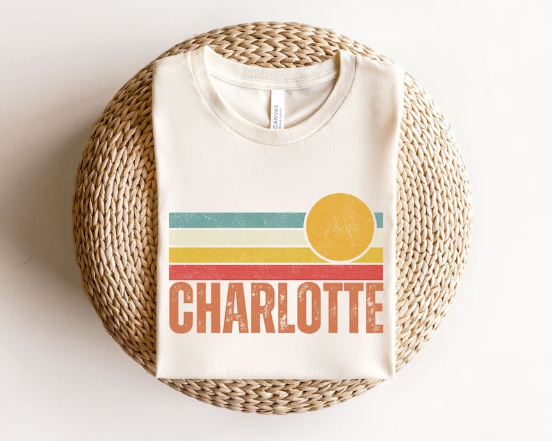 May include: A white t-shirt with a retro sunset graphic and the name "CHARLOTTE" printed in orange.