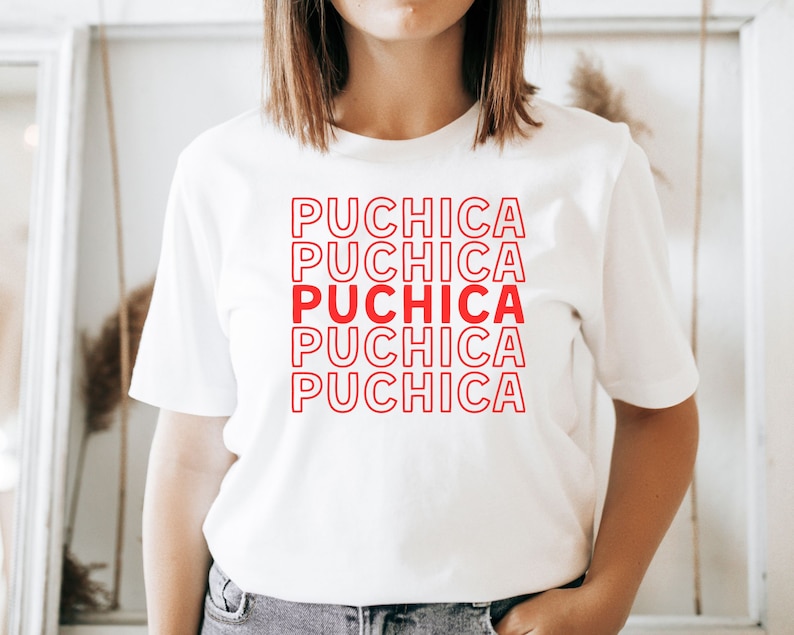 Puede incluir: Camiseta blanca con la palabra "Puchica" repetida cinco veces en texto rojo con contorno.