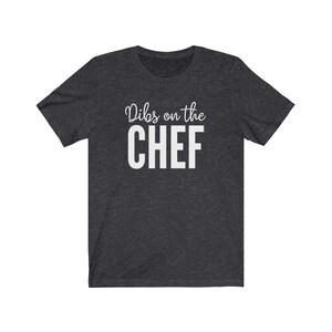 May include: A dark heather grey t-shirt with the text "Dibs on the CHEF" printed in white.