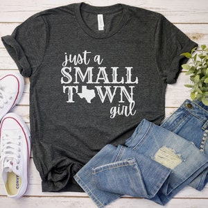 May include: A dark gray t-shirt with the text "just a SMALL TOWN girl" in white lettering. The text includes a white outline of the state of Texas.