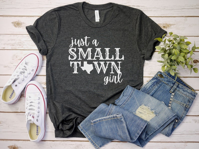 May include: A dark gray t-shirt with the text "just a SMALL TOWN girl" in white lettering. The text includes a white outline of the state of Texas.