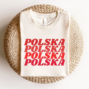 May include: A white t-shirt with the word "POLSKA" repeated four times in a red gradient, with each word slightly offset from the one above it.