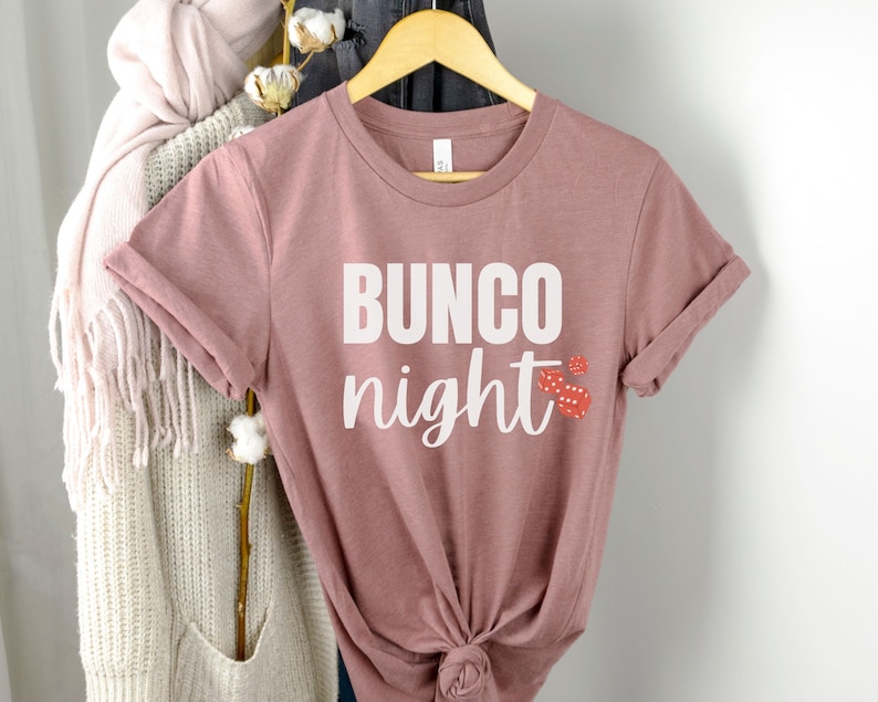 May include: A mauve t-shirt with the text "BUNCO night" in white lettering and red dice graphics.