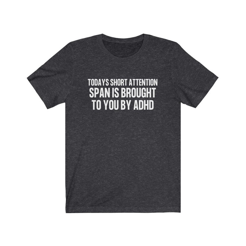 K&ouml;nnte beinhalten: Ein dunkelgraues T-Shirt mit dem Aufdruck "TODAYS SHORT ATTENTION SPAN IS BROUGHT TO YOU BY ADHD" in wei&szlig;.