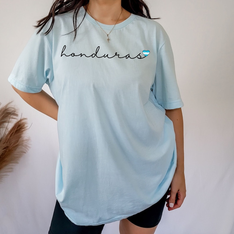 May include: A light blue t-shirt with the word "honduras" written in black cursive script and a small blue and white heart with a Honduran flag design.