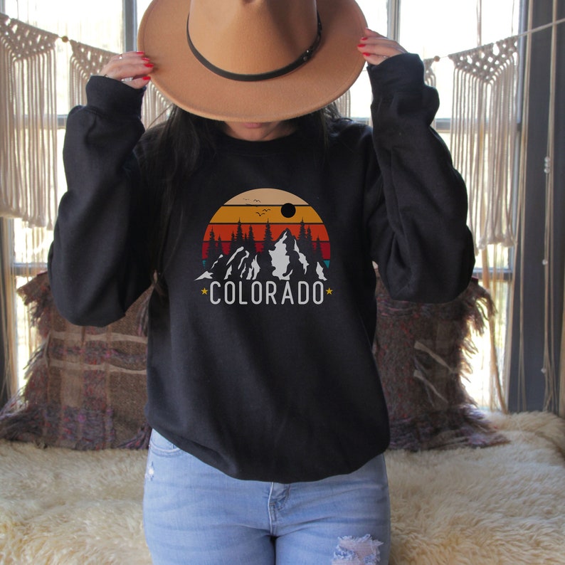 May include: A black sweatshirt with a retro-style graphic of mountains, trees, and a sunset. The graphic includes the text "*COLORADO*" in white.