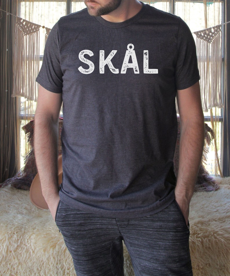 Puede incluir: Una camiseta gris oscuro jaspeada con la palabra "SK&Aring;L" impresa en blanco en la parte delantera. La palabra est&aacute; en una fuente desgastada.