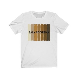May include: White t-shirt with a horizontal stripe design in shades of brown. The word "SALVADORE&Ntilde;A" is printed in black letters on the shirt.