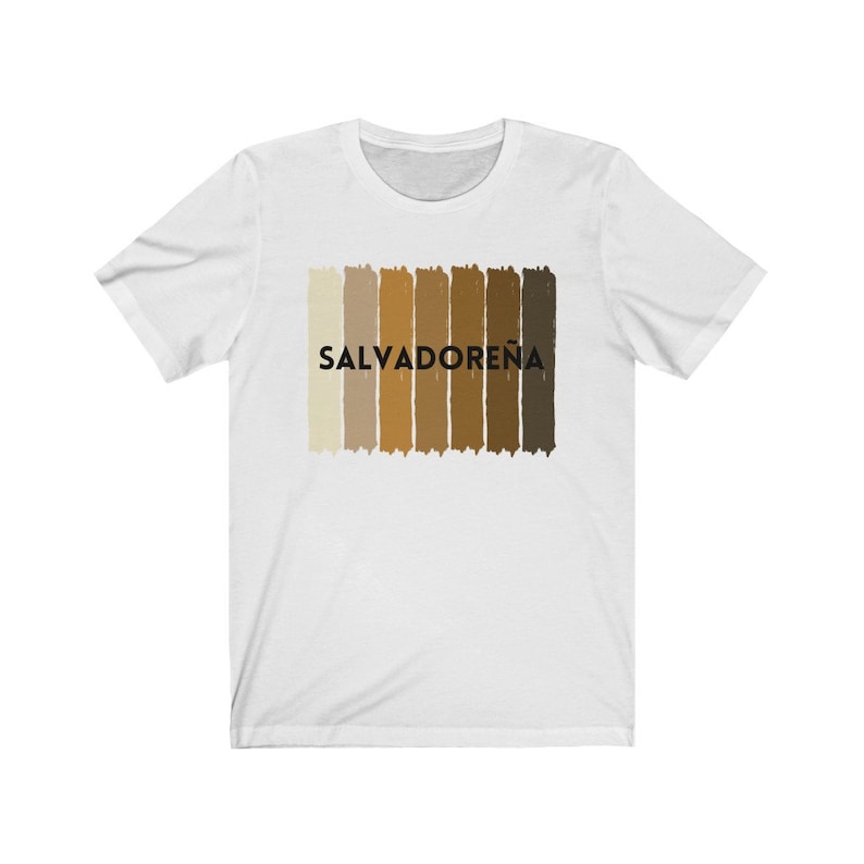 May include: White t-shirt with a horizontal stripe design in shades of brown. The word "SALVADORE&Ntilde;A" is printed in black letters on the shirt.
