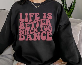 Könnte beinhalten: Schwarzer Pullover mit einem rosafarbenen Aufdruck, der in einer Retro-Schrift "Life is better when you dance" sagt.