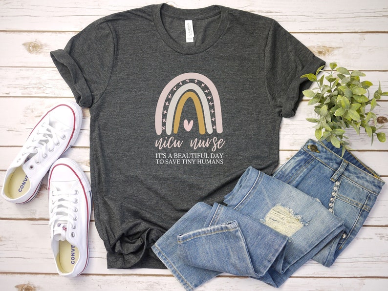 May include: A dark gray t-shirt with a rainbow design and the text "NICU NURSE IT'S A BEAUTIFUL DAY TO SAVE TINY HUMANS".