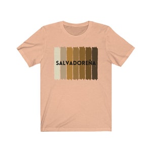 May include: A peach-colored t-shirt with a graphic of a horizontal stripe pattern in shades of brown and beige. The text "SALVADORE&Ntilde;A" is printed in black below the stripes.