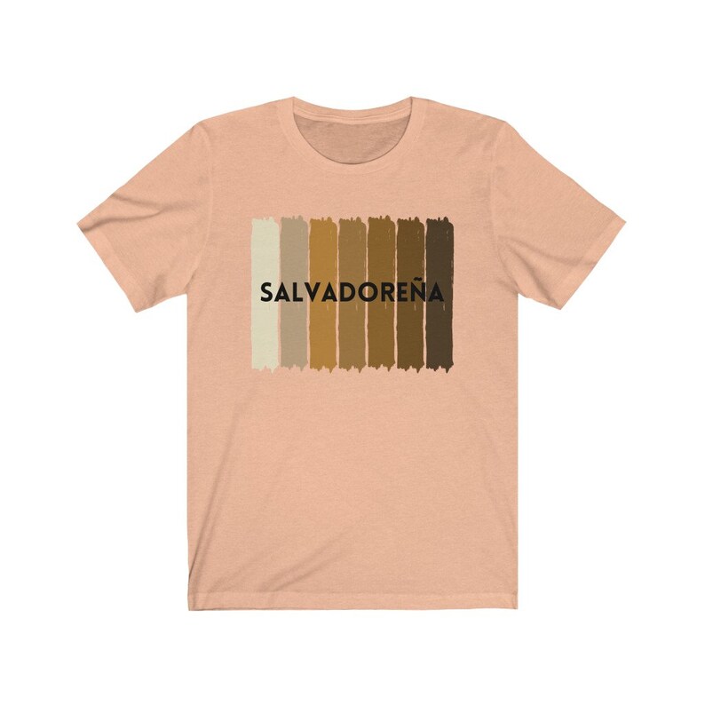 May include: A peach-colored t-shirt with a graphic of a horizontal stripe pattern in shades of brown and beige. The text "SALVADORE&Ntilde;A" is printed in black below the stripes.