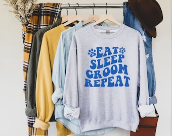 May include: A gray sweatshirt with a blue graphic that says "Eat Sleep Groom Repeat" with paw prints on either side of the text.