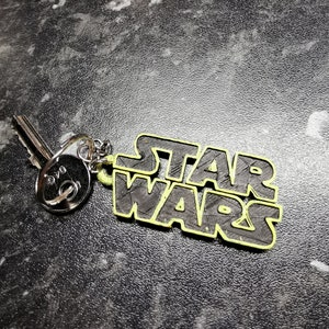 May include: A black and yellow Star Wars keychain with a silver key attached.