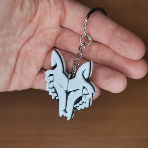 May include: White plastic keychain with a double wolf head design. The keychain is attached to a silver metal ring.