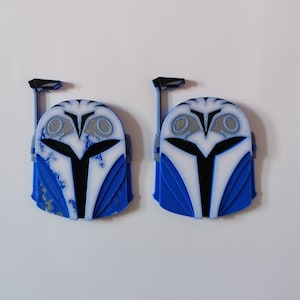 May include: Two blue and white Mandalorian helmets with a weathered paint effect. The helmets have a black visor and a black antenna on top.