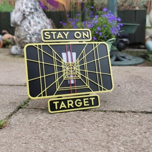 May include: A black and yellow metal sign with the words "Stay on Target" and a graphic of a targeting system.
