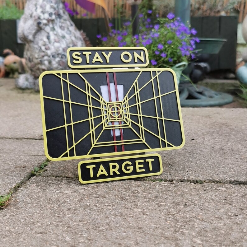 May include: A black and yellow metal sign with the words "Stay on Target" and a graphic of a targeting system.