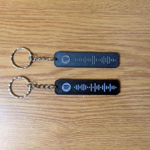 May include: Two black keychains with silver key rings. Each keychain has a black and white Spotify barcode with the Spotify logo.