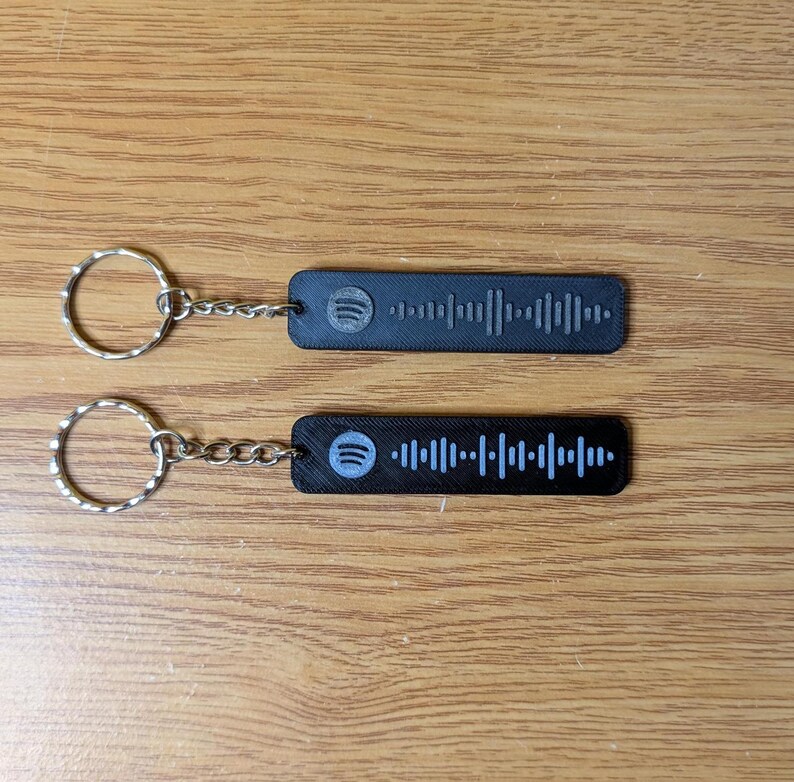 May include: Two black keychains with silver key rings. Each keychain has a black and white Spotify barcode with the Spotify logo.