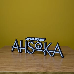 May include: A black and white 3D printed sign that reads "STAR WARS AHSOKA" with a stylised font.