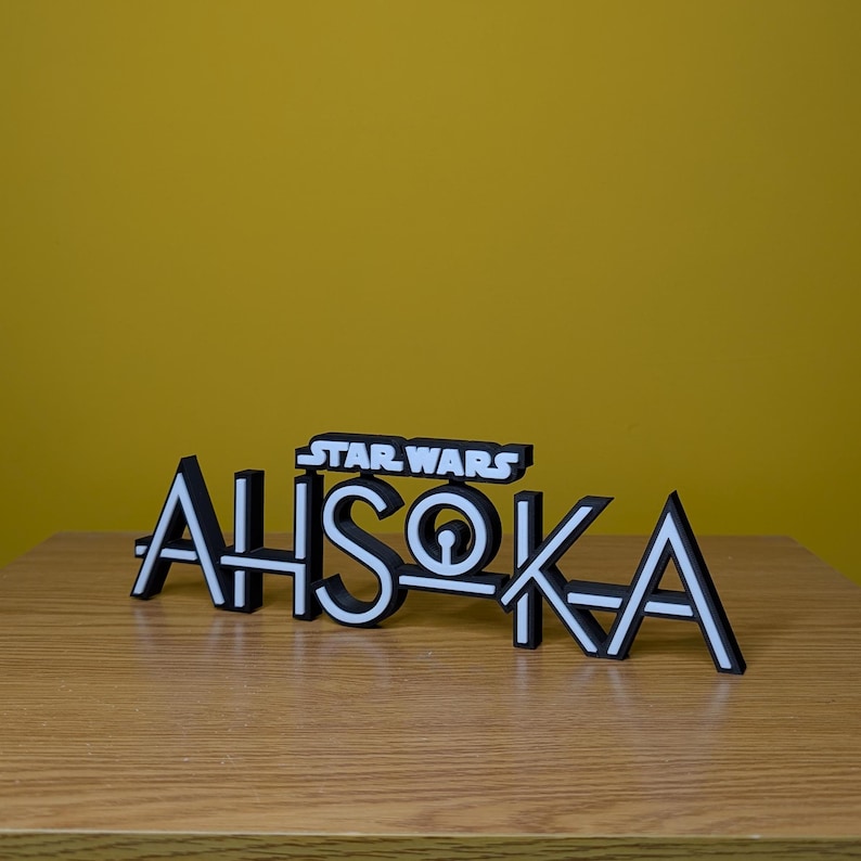 May include: A black and white 3D printed sign that reads "STAR WARS AHSOKA" with a stylised font.