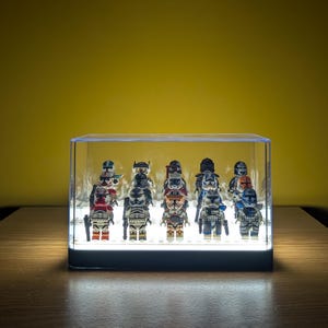 May include: A clear acrylic display case with a light inside, showcasing a collection of 12 Star Wars Clone Trooper minifigures. The figures are arranged in a row, facing forward, and are all wearing different armour and helmets.