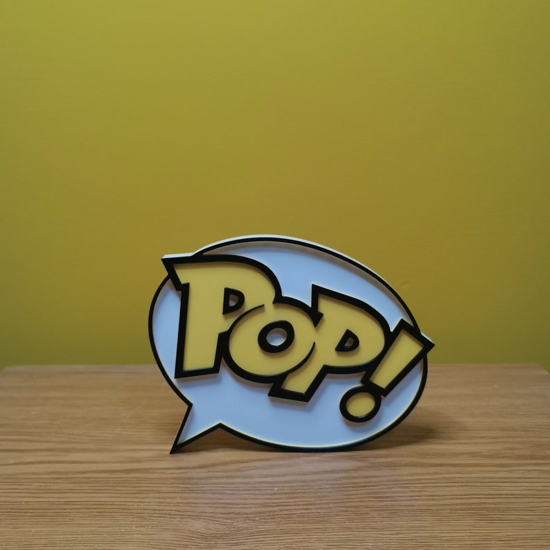 May include: A white speech bubble with a black outline and the word "Pop!" in yellow letters. The letters are in a bold, cartoon-style font.
