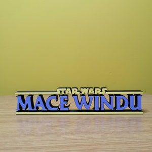 May include: A black and yellow 3D printed sign with the text "STAR WARS MACE WINDU" in blue letters.