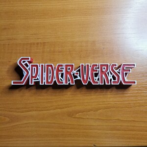 May include: A 3D printed red and white sign with the text "SPIDER-VERSE" in a bold, stylized font.