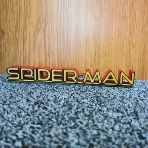 May include: A red and gold plastic sign with the words "SPIDER-MAN" in black letters.