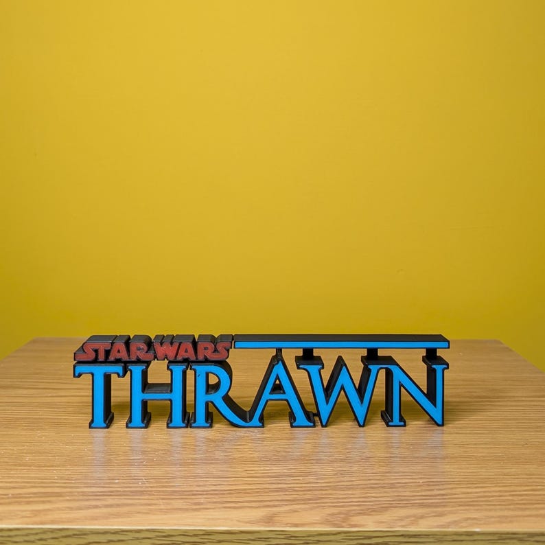 May include: A 3D printed sign with the words "STAR WARS" in red and "THRAWN" in blue. The sign is made of black plastic and has a blue stripe across the top.