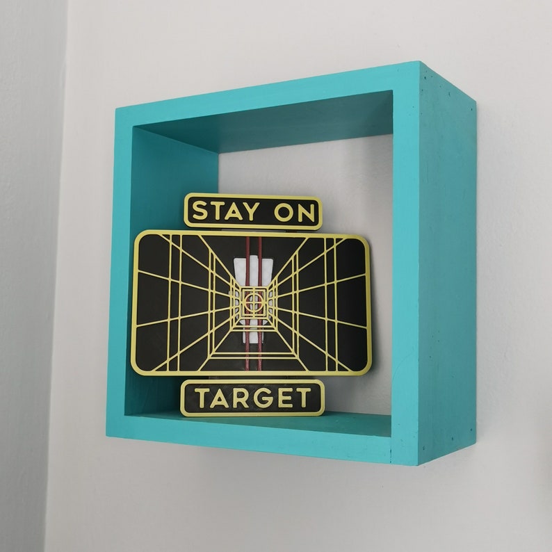 May include: A turquoise blue wooden frame with a black and gold graphic inside. The graphic is a stylized image of a target with the text "Stay on Target".