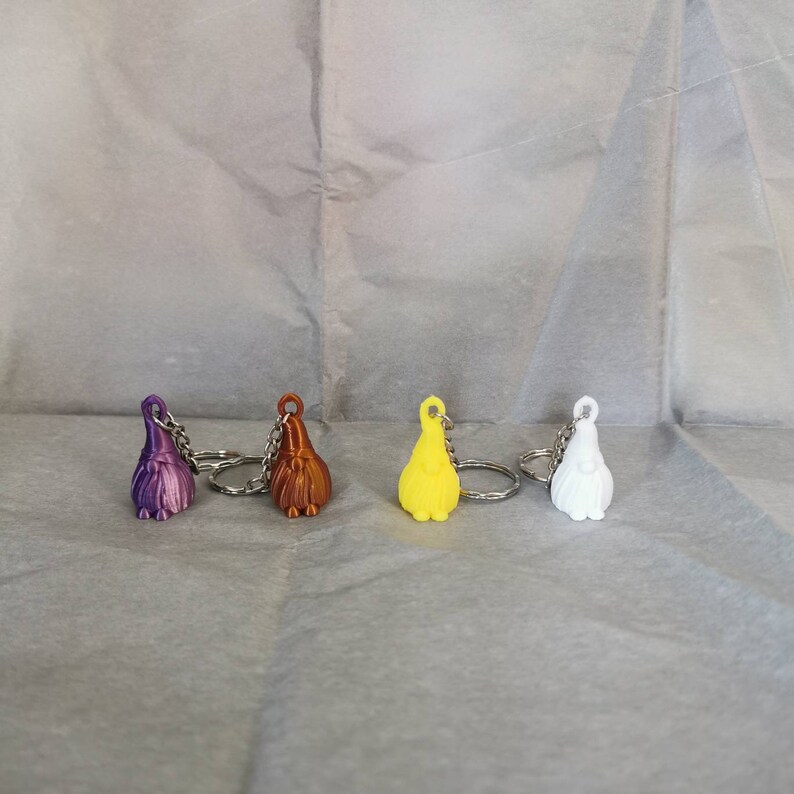 May include: Four colourful gnome keychain ornaments with silver key rings. The gnomes are purple, brown, yellow, and white.