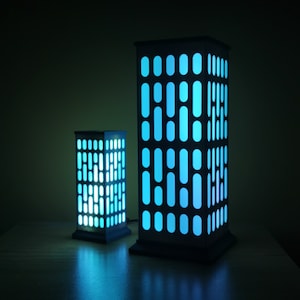 May include: Two black and white lamps shaped like buildings with blue light shining through the windows.
