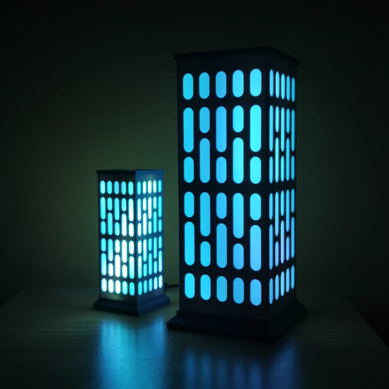 May include: Two black and white lamps shaped like buildings with blue light shining through the windows.
