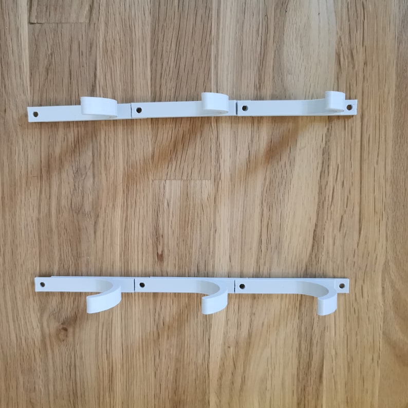 May include: Two white metal wall mounted towel racks with three hooks each. The racks are mounted on a light brown wood surface.