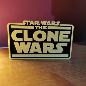 May include: A black and yellow sign with the text "Star Wars The Clone Wars" in a bold, white font.
