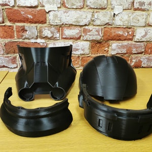 Puede incluir: Un casco de pl&aacute;stico negro desmontado en cinco piezas. El casco est&aacute; formado por una c&uacute;pula, una pieza frontal y tres piezas m&aacute;s peque&ntilde;as que se conectan a la c&uacute;pula y a la pieza frontal.