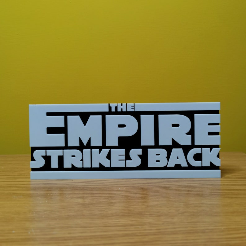May include: A white sign with black lettering that reads "THE EMPIRE STRIKES BACK".