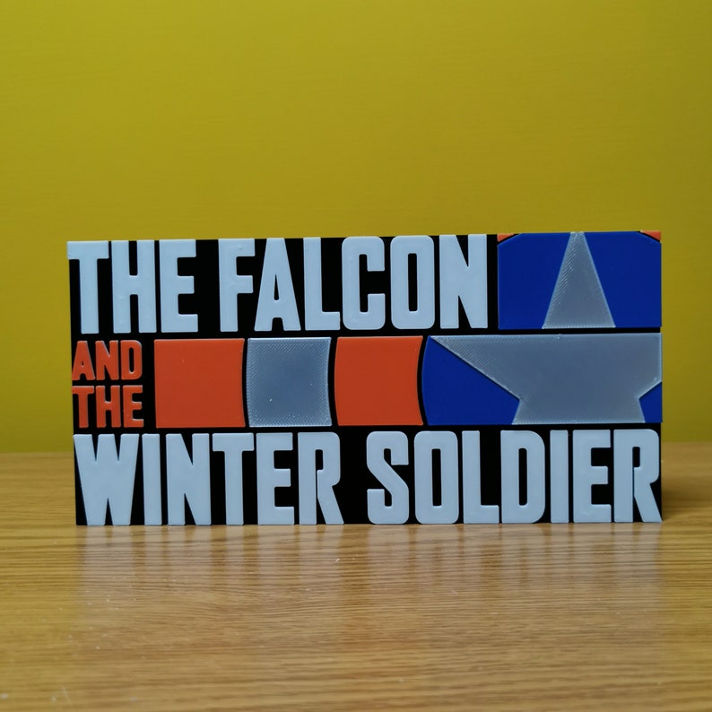 May include: A black and white sign with the text "The Falcon and the Winter Soldier" in white letters. The sign also features a red, white, and blue design with a star.