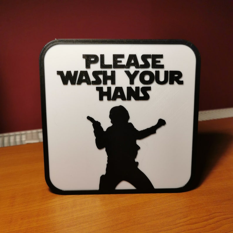 K&ouml;nnte beinhalten: Ein wei&szlig;es Schild mit schwarzem Rand und schwarzem Text, der "Please Wash Your Hans" lautet, mit einer Silhouette von Han Solo aus Star Wars, der einen Blaster h&auml;lt.